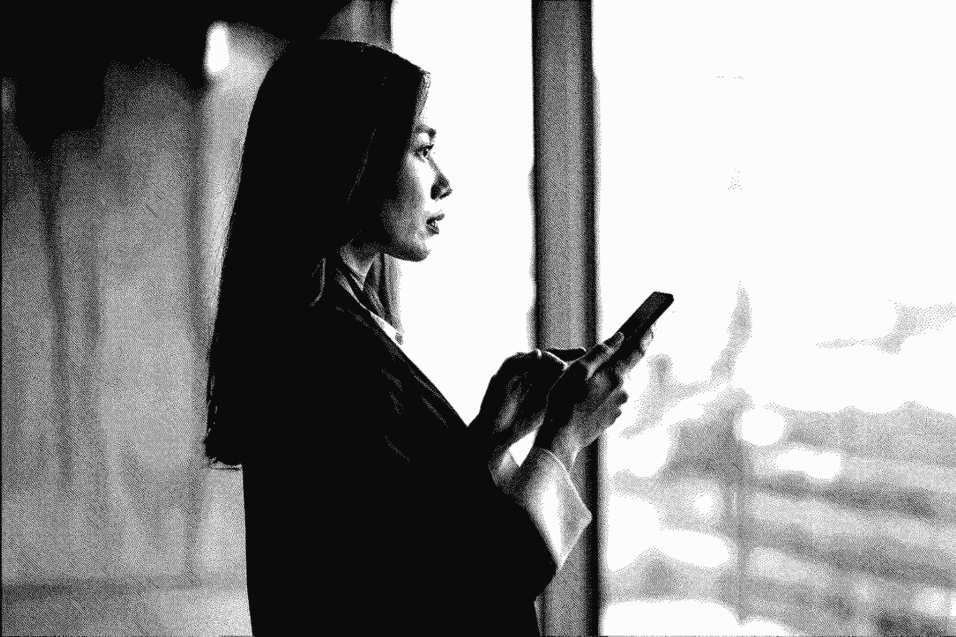 A professional checking her smartphone in front of the glass façade of an office building