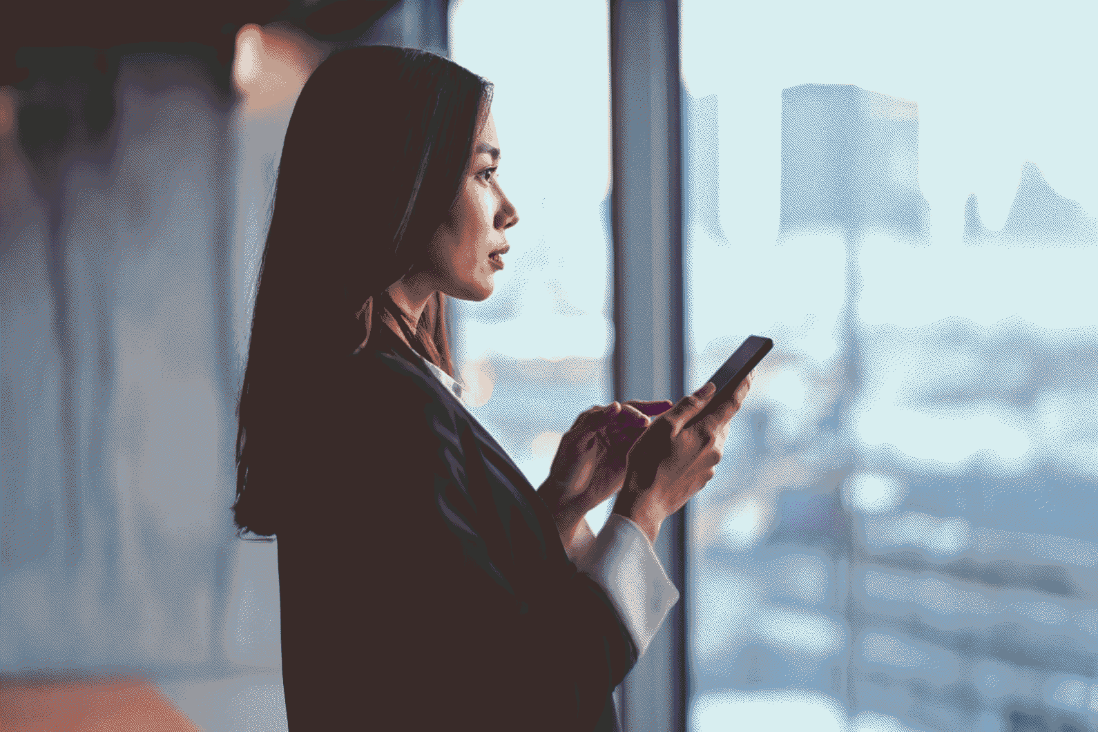 A professional checking her smartphone in front of the glass façade of an office building